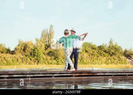 Senior couple holding hands while dancing on jetty Stock Photo