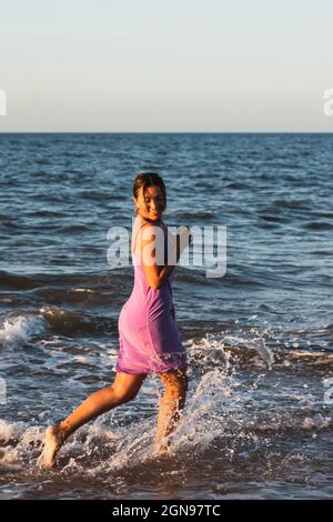 Playful woman splashing water while running on beach Stock Photo