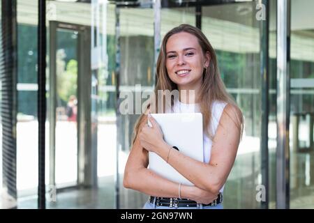 Smiling female freelancer holding laptop while standing at entrance Stock Photo