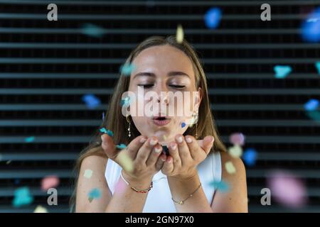 Businesswoman blowing confetti in front of black wall Stock Photo