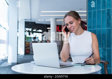 Female graphic designer talking on mobile phone in coffee shop Stock Photo