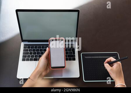 Female graphic designer using mobile phone and graphic tablet on cafe table Stock Photo