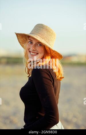 Smiling redhead woman wearing hat at sunset Stock Photo