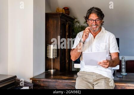 Smiling businessman checking document while leaning on desk at home office Stock Photo