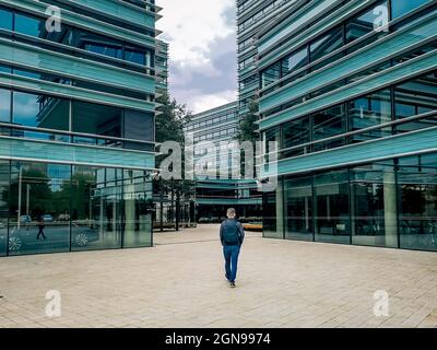 Man in jeans, jacket and backpack goes to a modern office building Stock Photo