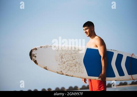 Young man holding his surfboard on the beach. Stock Photo