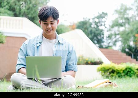 Collage student using laptop sitting at the campus yard, online study concept. Stock Photo