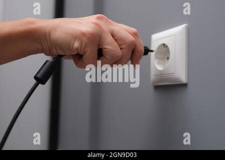 Woman hand inserts electrical plug into outlet closeup Stock Photo