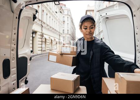 Delivery worker unloading cardboard boxes while standing at van trunk Stock Photo