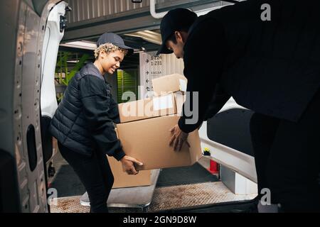Two couriers stack cardboard boxes in a delivery van. Coworkers pick up the packages from the warehouse. Stock Photo