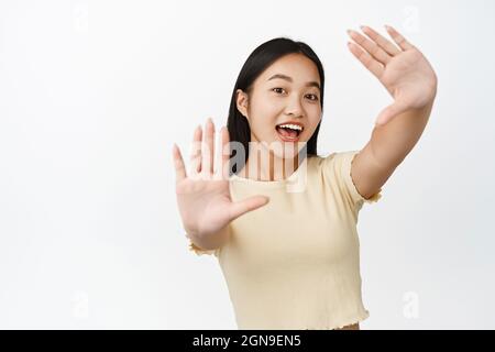 Excited asian female model, looking through hand frames, laughing and smiling happy, imaging something, standing over white background Stock Photo