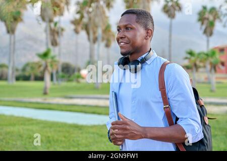 Outdoor portrait of young man with laptop headphones and backpack Stock Photo