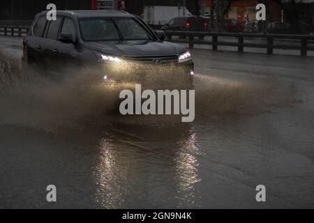 The car is driving in a puddle. Sprays from under the wheels. A flooded highway. Transport with lights turned on goes on the highway. Stock Photo
