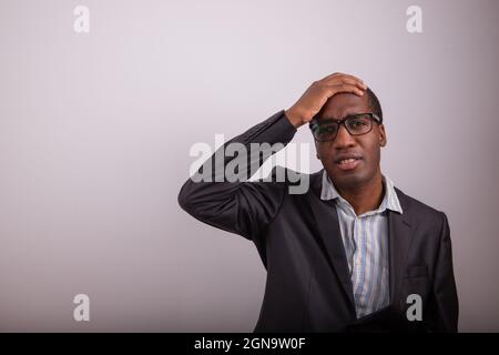 African businessman has a confused expression, he puts his hand on his head and is disoriented. Man with eyeglasses and lost expression, copy space Stock Photo