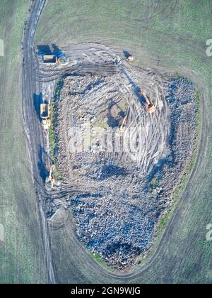 Construction site aerial view with heavy equipment, earth movers, dump trucks working on surface excavation in a green field, Victoria, Australia. Stock Photo