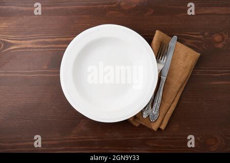 Empty white circle ceramic plate on wooden background with silverware and linen napkin Stock Photo
