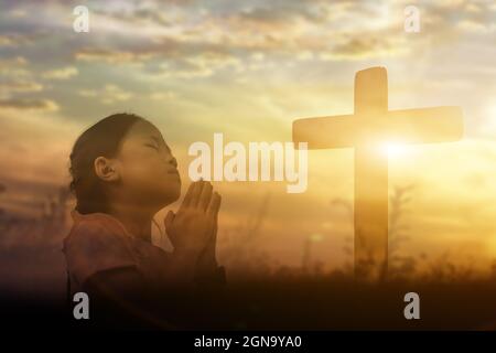Young girl raising hands worship and praise God at sunset background. Christian Religion concept. Stock Photo