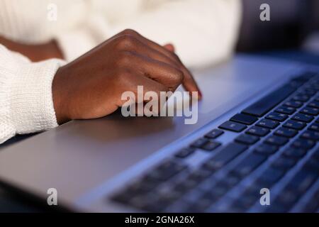 Close-up of african american businesswoman hands hand typing company strategy on laptop computer late at night in startup corporate office. Executive manager reading financial statistics document Stock Photo