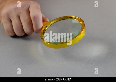 Man's hand holds magnifying glass over gray surface. Larger loup Stock Photo