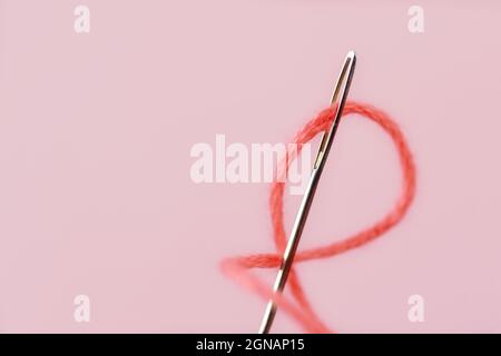 Close-up of sewing needle eye with pink thread Stock Photo