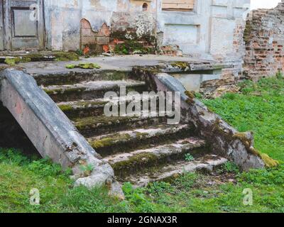 Stone stairs are falling apart. Old steps covered by green moss and lichens. Destroyed entrance of a former manor house Stock Photo