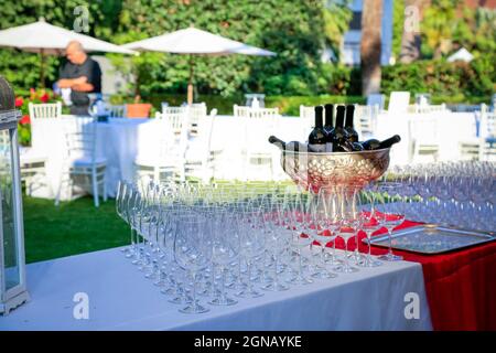 many crystal wineglasses and red wine in a metal vase on buffet table in garden. Blurred background. Wine tasting preparation. Wedding party Stock Photo