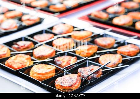 set of small black square dishes with fingerfood. backed oriental snacks with tiny spoons. Catering layout. Gourmet food degustation. Menu concept Stock Photo