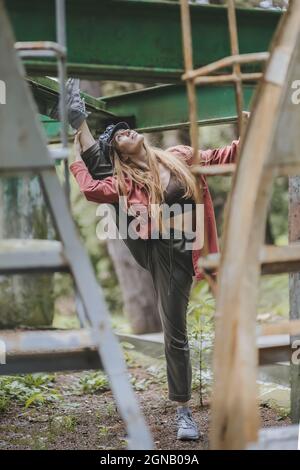 A woman in casual outfit doing a stretch with her leg thrown over the bar of a metal structure outdoors on a summer day Stock Photo