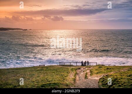 A family of holidaymakers standing on Towan Head looking out as the sun sets over Fistral Bay in Newquay in Cornwall UK. Stock Photo