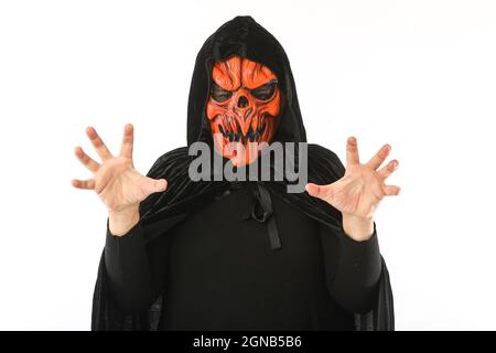 Man dressed in pumpkin latex mask and hooded velvet cape, scares with his hands, on white background. Carnival, Halloween and days of the dead concept Stock Photo