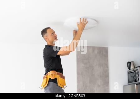 Worker repairing lamp on stretch ceiling indoors Stock Photo