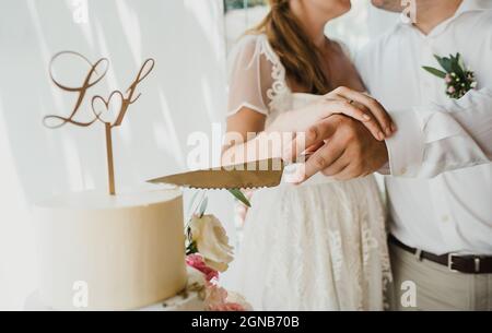 Crop newlyweds cutting wedding cake together Stock Photo