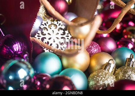 Wooden snow flake in present red bag on multicolour Christmas balls. Sparkling colourful new year tree toys. Holiday background composition. Flat Stock Photo