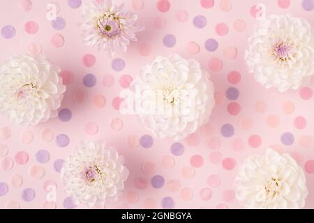 Trendy abstract image of white flowers with colorful round paper confetti on trendy pink background in flat lay style for decoration design. Beautiful pink gift card with copy space. Holiday concept.