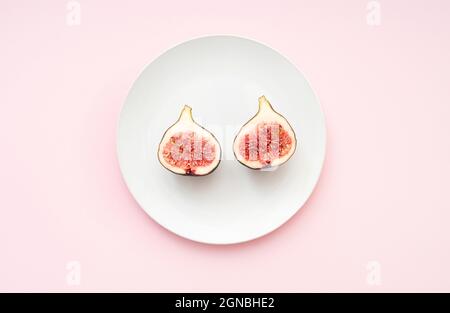 Minimal composition with two parts of figs on a white ceramic plate. Plate with fig on pink surface, top view Stock Photo