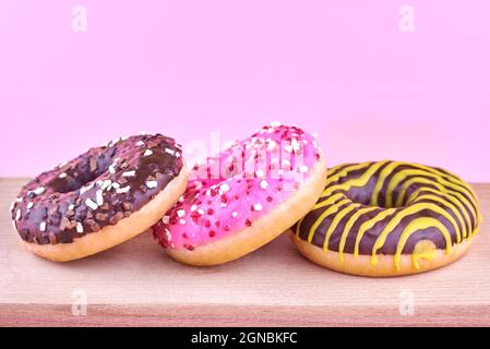 Three bright donuts on a wooden board on a pink background. Stock Photo