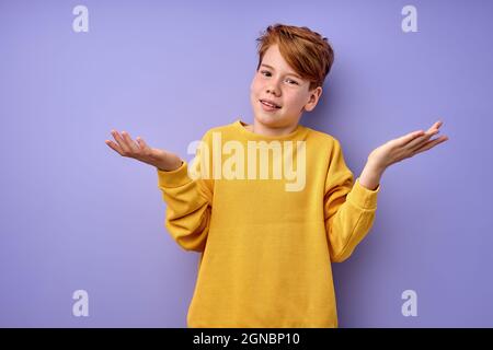 young caucasian boy is misunderstanding what happened, shrugging, spreading arms at side, looking at camera with confused facial expression. portrait Stock Photo