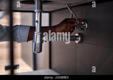Handsome Hardworking Plumber Installing The Sink In Bathroom Close-up Photo, Cropped Black Man. Guy Is Repairing, Fixing Sink. Skilled Handyman During Stock Photo