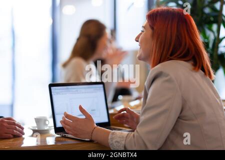 Happy red hair businesswoman at a cafe with a tablet tablet talking to someone. Stock Photo