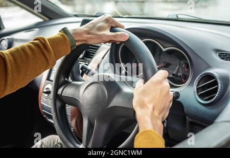 Male hands are holding the steering wheel close up. Man in a yellow sweater is driving a car. Concept of travel. Stock Photo