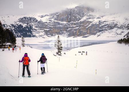 Two people walking with snowshoes in snowy mountain landscape with frozen lake on background Stock Photo