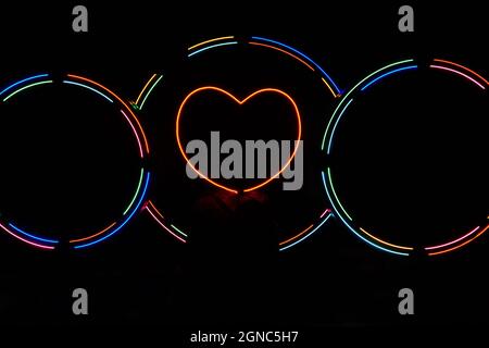 Red neon heart on black background decorated with multicolored neon light. Two empty circles for names. Illuminated heart decoration. Horizontal photo Stock Photo
