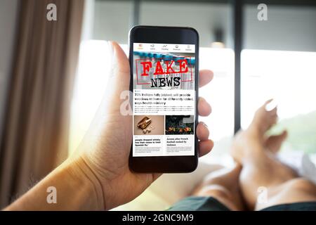 Man reading fake news or articles about covid-19 in a smartphone screen application. Mockup app website. Fake Newspaper portal. Media technology. Stock Photo