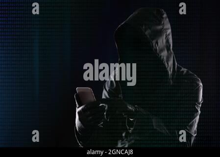 Hacker in a dark hood hacks into a modern mobile phone on the background of binary code, Internet personal data security concept Stock Photo