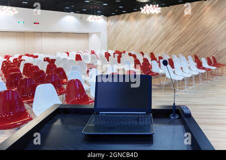 A laptop computer at a podium and rows of chairs in a large room Stock Photo