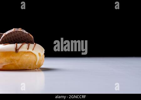 Part of a white chocolate donuts with dark chocolate cookies on a white table and a black background.The photo is taken in horizontal format and has c Stock Photo
