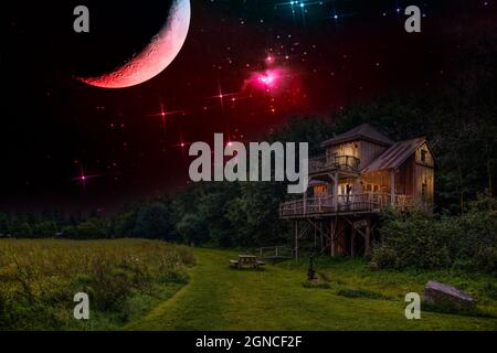 Night scene of a tree house on a forest edge and path along meadow with warm yellow lamplight shining through the windows Stock Photo