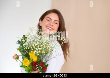 happy girl with a bouquet of flowers in armful on light background Stock Photo