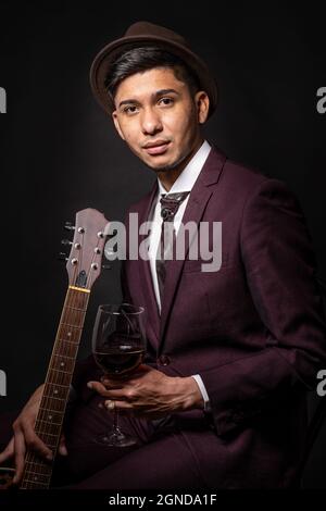 Caucasian man from Spain in suit and hat holding a guitar, sitting and looking at camera Stock Photo