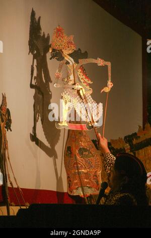 A Dalang of Javanese shadow puppet was lifting one of the puppet characters so that it casts a shadow on the white screen. Stock Photo